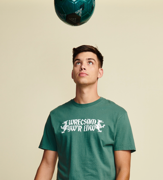 Photo from waist up of male model wearing green welsh "Wrecsam" shirt in white text. Bookended with white dragon graphics.Short Sleeve