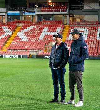 Photo of Rob Mcelhenney and Ryan Reynolds standing on Racecourse pitch. 