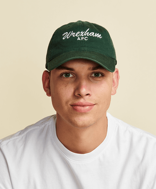 Close up photo of male model wearing green dad hat that reads "Wrexham" white script text.