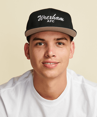 Photo of male model wearing a black flat brim hat with wrexham afc embroidered in white in a script font
