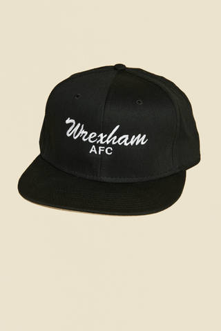Product Photo: flat brim hat, black with "Wrexham" written in Script font, text is white.